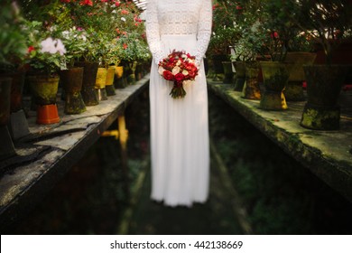 Intentionally Blurred Image Of A Bride In White Simple Dress Hold A Bouquet Of Red Flowers In Her Hands. Tilt-shift Lens Used, Soft Selective Focus.