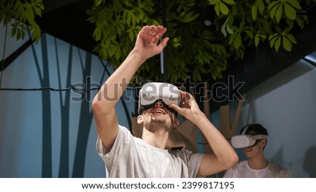 Interactive experience in the virtual reality room, two male students using VR glasses, looking around the space and moving arms through the air.