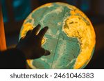 Interactive Geography: Searching for a Country.Exploring the World: A hand reaches out to a glowing globe in a dark room. Educational Journey: Luminous Globe and Seeks Out Names of Countries.