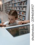 Interactive information search system in the library. A schoolgirl is in the library, looking for information on the computer.
