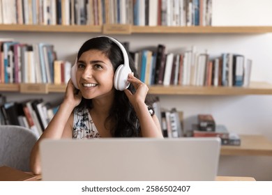 Interactive virtual learning. Confident young girl remote student in headset sit by notebook at library repeat after teacher at foreign language audio web course listen to webinar podcast. Copy space