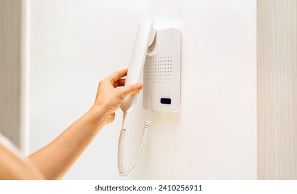 Intercom handset in female hand. Intercom on white wall with copy space.