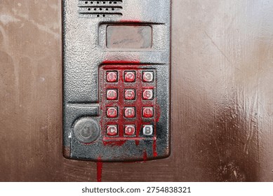  Intercom panel covered in red paint resembling blood. Concept of crime, danger, or vandalism.  Vandalized door phone system on a metal door. Red spray paint streaks on an apartment intercom.