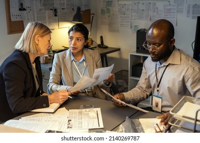 Intercultural Agents Of FBI Discussing Information Of Main Suspects In Their Criminal Profiles While Male Detective Reading Document