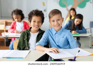 Intercultural schoolkids boys sitting at desk during lesson, looking at camera and smiling - Powered by Shutterstock