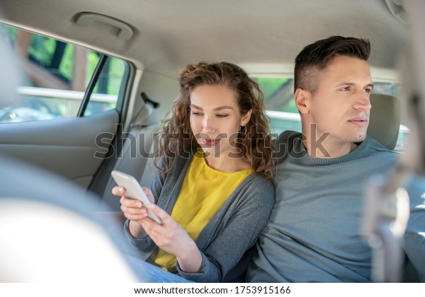 Interest,\
observation. Smiling woman with smartphone and interested man\
looking out the car window by turning his\
head