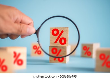 Interest rate financial and mortgage rates concept. In the hand of a businessman holding a magnifying glass choose wooden cube block with icon percentage symbol on blue background. - Powered by Shutterstock