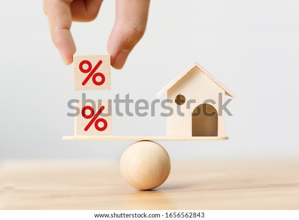 Interest rate financial and mortgage rates\
concept. Wooden home and hand putting cube block shape with icon\
percent on wood scales