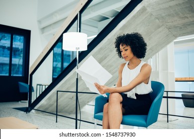 Interested african american businesswoman checking financial reports with information data working in lounge room of own company, concentrated female entrepreneur reading paper documents indoors