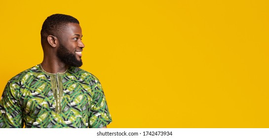Interested african man in traditional costume looking at copy space over yellow background, panorama
