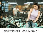 Interested avid female cyclist choosing new bike for cycling trips in busy store, carefully picking comfortable bicycle saddle