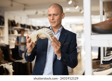 Interested bald man choosing new comfortable shoes in store, checking softness of sole of moccasins