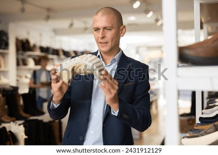 Interested bald man choosing new comfortable shoes in store, checking softness of sole of moccasins