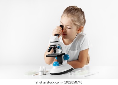 Interested child girl looks through a microscope on a white background. Micro biology for young children. - Powered by Shutterstock