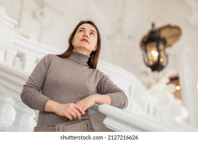 Interested female tourist admiring sumptuous interiors of antique palace while standing on stairs near white stucco railings, selective focus - Shutterstock ID 2127216626