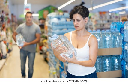 Interested Focused Young Hispanic Woman Reading Label On Bottle Of Still Water While Shopping In Supermarket