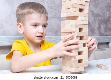 Interested Happy Little Blond Boy Playing Board Game Taking Bricks From Wooden Tower Keeping Balance