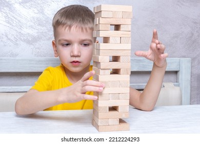 Interested Happy Little Blond Boy Playing Board Game Taking Bricks From Wooden Tower Keeping Balance. Board Game Tower Of Wooden Blocks. Activity For Strategy, Concentration, Agility