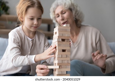 Interested Happy Small Red Head Kid Girl Playing Board Game With Joyful Middle Aged Mature Grandmother, Taking Bricks From Wooden Tower Keeping Balance, Having Fun Entertaining Together At Home.