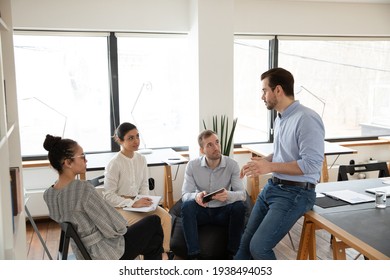 Interested happy young multiracial colleagues sitting on chairs, listening to male boss team leader, explaining working issues at briefing meeting in modern office, international company collaboration - Shutterstock ID 1938494053