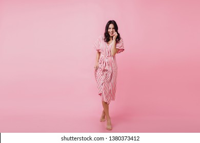 Interested joyful woman in dress posing in studio. Enchanting sensual girl standing on pink background