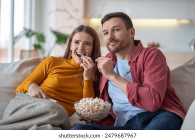 interested married couple wife husband hooked on movie. Family pastime, leisure, watch television, rest. Relaxed man woman watching TV series together sitting on couch at home enjoying eating popcorn. - Powered by Shutterstock