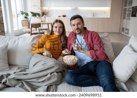 interested married couple wife husband hooked on movie. Family pastime, leisure, watch television, rest. Relaxed man woman watching TV series together sitting on couch at home enjoying eating popcorn.