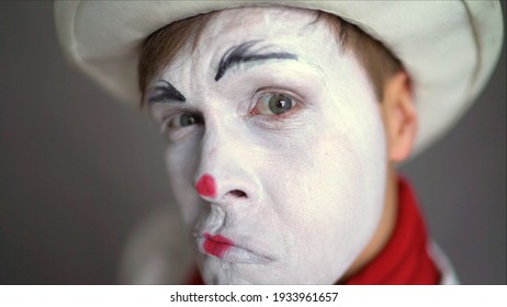 Interested in pantomime. Portrait of an actor as a pantomime with a white face makeup, showing expressive emotions on a background in the studio.