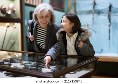 Interested Preteen Girl Visiting History Museum Of With Grandmother, Viewing Ancient Handguns In Glass Display Case