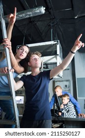 Interested Teen Boy With His Mother Reaching For Something In Quest Room Designed As Underground Shelter, Trying To Find Clue