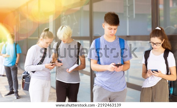 Interested teenagers carried away with their\
smartphones on college campus during break in lessons. Generation Z\
of digital natives\
concept