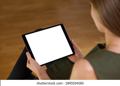 Interested Woman Sitting And Holding Tablet With Blank White Screen In Her Hands. Back View Of A Female Using Large Mobile Device For Reading And Analyzing.