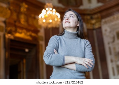 Interested woman tourist admiring sumptuous interiors of medieval palace decorated with gold and antique chandelier in blurred background.. - Shutterstock ID 2127216182
