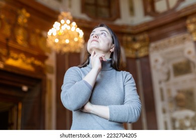 Interested woman tourist admiring sumptuous interiors of medieval palace decorated with gold and antique chandelier in blurred background.. - Shutterstock ID 2232704205