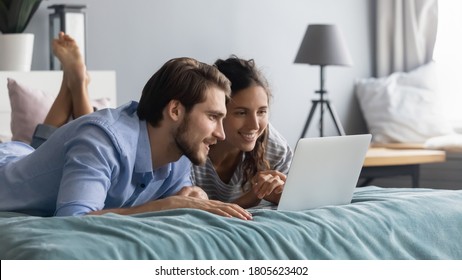 Interested young couple lying on cozy bed, looking at computer screen. Relaxed man planning vacating with beloved woman , web surfing information on computer in bedroom, family weekend pastime concept - Powered by Shutterstock