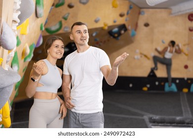 Interested young girl and man standing near bouldering wall in climbing gym, engaged in conversation. Coach instructing beginner female climber about specific moves or technique - Powered by Shutterstock