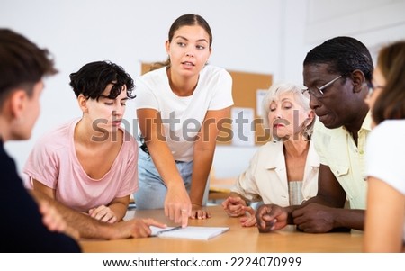 Interested young girl participating in Spanish language speaking club, communicating with multiracial group of people of different ages sitting around table..