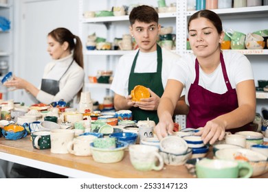 Interested young man and women in aprons viewing handmade clay products on the table in pottery workshop - Powered by Shutterstock