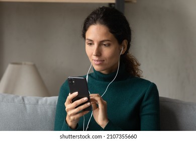 Interested young woman in wired earphones listening educational lecture online on smartphone, studying distantly on internet courses. Happy millennial lady holding video call conversation at home. - Shutterstock ID 2107355660