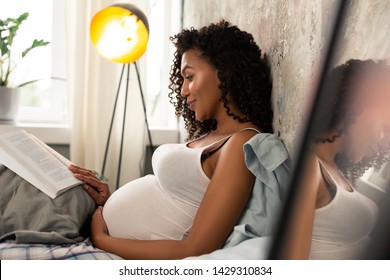 Interesting book. Happy expectant mother with a book reclining on a pillow in her bed. - Powered by Shutterstock