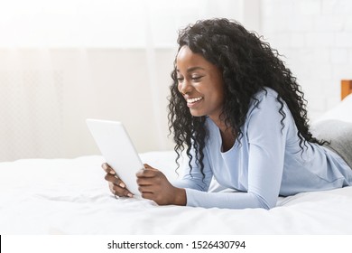 Interesting content. Millennial african girl reading blog on digital tablet lying in bed, free space