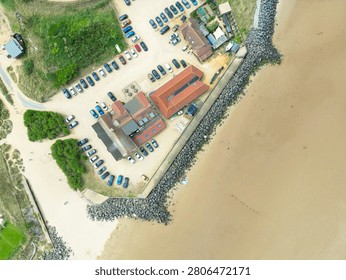 Interesting drone top down view of an English Golf Club and outbuildings seen on north Norfolk, UK coastal town of Brancaster. Flood defensive boulders around the perimeter can be seen and the wide beach at low tide.