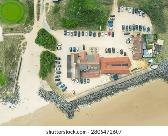 Interesting drone top down view of an English Golf Club and outbuildings seen on north Norfolk, UK coastal town of Brancaster. Flood defensive boulders around the perimeter can be seen and the wide beach at low tide.