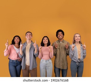 Interesting offer from students, great ad and modern pupils advice. Smiling zoomers multiracial people pointing thumbs up and looks on empty space, isolated on orange background, studio shot, square