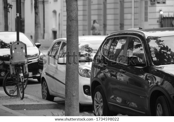 Interesting photo of black\
and white cars parked in paris. There is a bike and tree to give\
balance to photo.