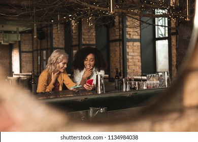 Interesting posts. Pleasant young women sitting at the bar counter and looking through social media timeline together while chuckling