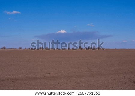 An interestingly shaped cloud over a plowed field.