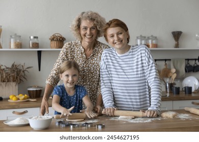 Intergenerational bonding, culinary traditions. Two generations of women and little girl cook, pose for camera, enjoy cookery, warm relations, creating lasting memories and connection through cooking - Powered by Shutterstock