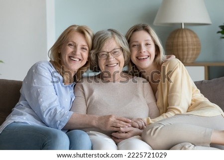 Intergenerational family portrait. Happy diverse women, elderly granny, mature daughter, millennial granddaughter smile pose for camera rest on sofa, enjoy time together, having good friendly relation