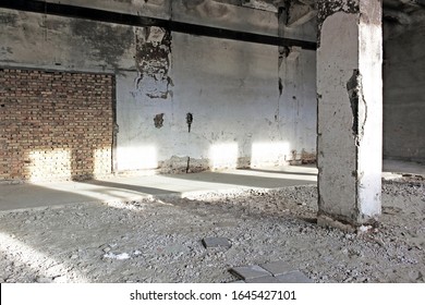 Interior of abandoned dusty concrete hall lit by sunlight with one big pillar and brick wall